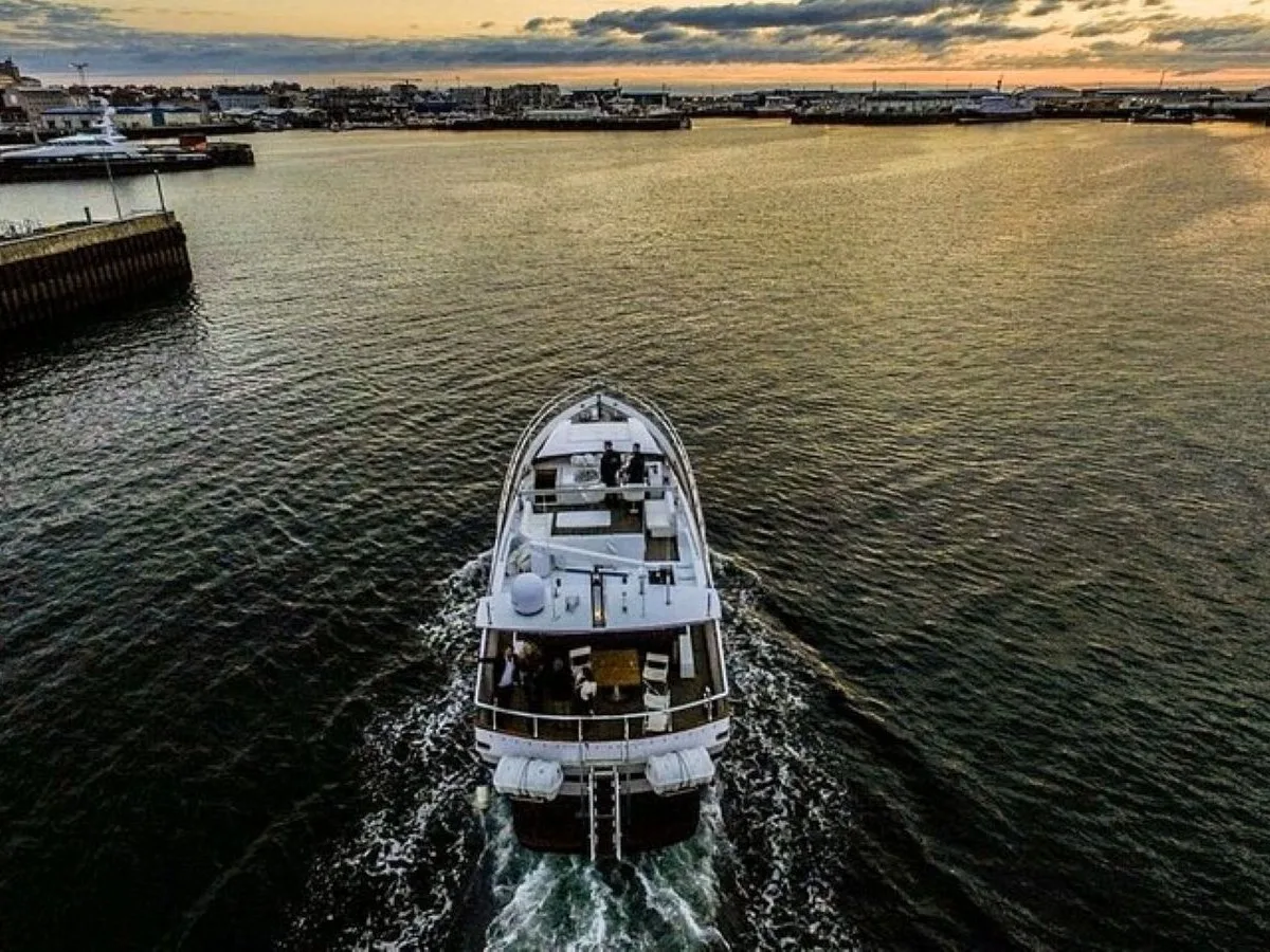 Aerial drone view of the Harpa yacht cruising through the Reykjavík Old Harbour at sunset during a premium sightseeing tour.
