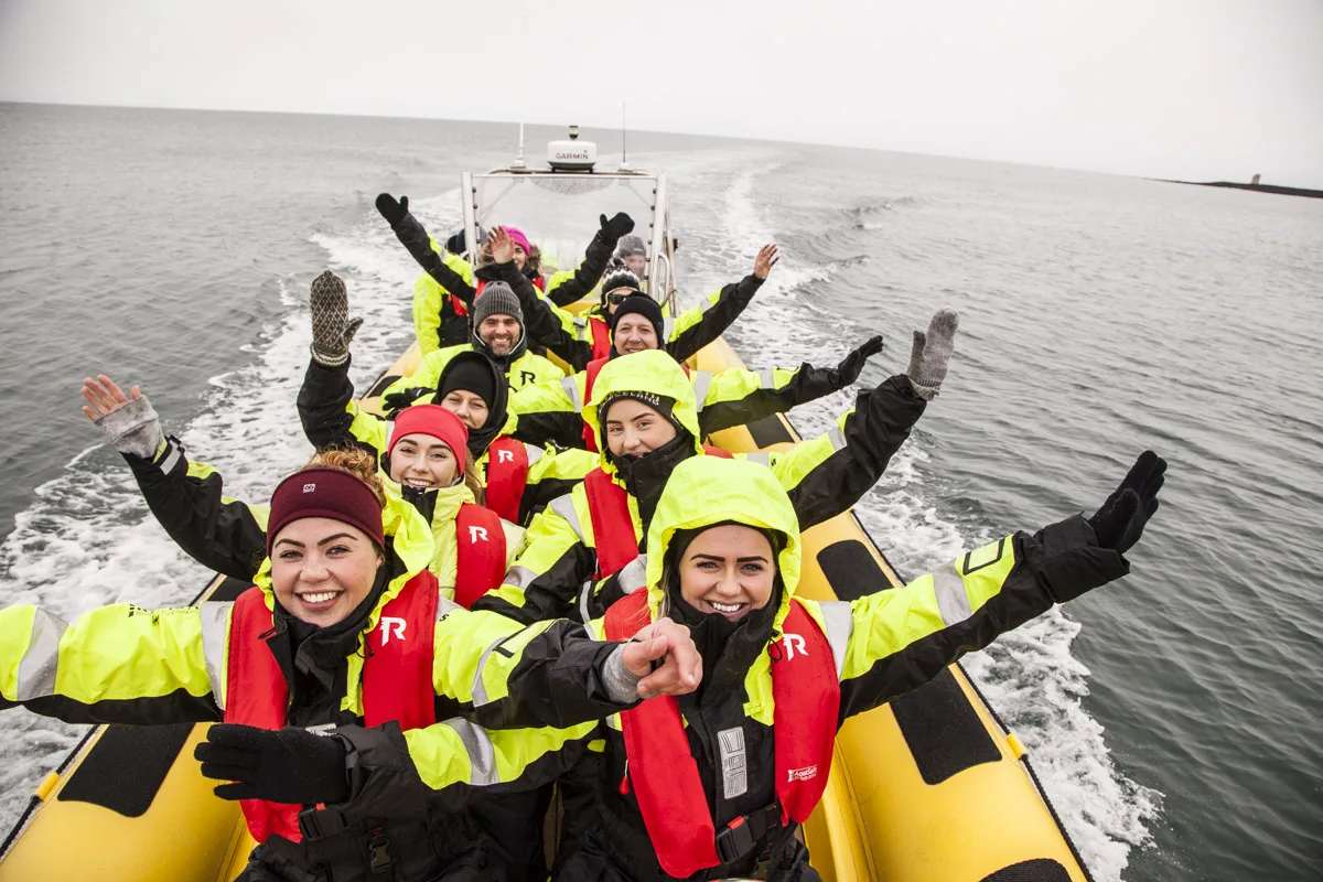 Happy passengers in protective thermal suits waving from a RIB speedboat during a whale watching tour in Reykjavík with Iceland Discover.